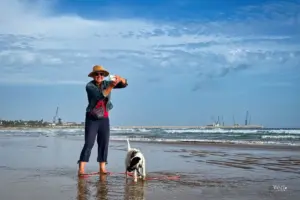 Eine Frau steht Barfuss am Strand im Wasser daneben ihr Hund