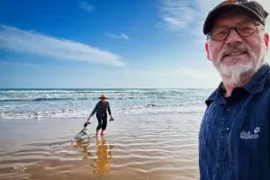 Grosser Sandstrand mit der Meeresbrandung bei schönem Wetter. Ein Hund ist mit seinen beiden Menschen am Strand