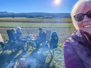 Ein paar Freunde sitzen draussen am Feuer in der Natur und geniessen gemeinsam ein Raclette.