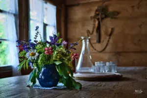 Tisch in einer Bauernstube aus dem 19. Jahrhundert dekoriert mit Blumen und einem Tablett mit einer Karaffe und Trinkgläser.