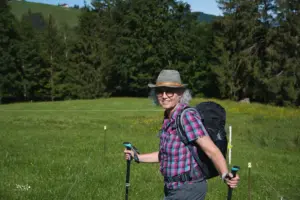 Eine Frau in Wanderausrüstung steht auf der Wiese über die der Wanderweg führt.
