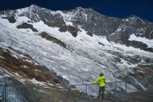 Ein Frau steht auf einer Aussichtsterasse in den Bergen und bestaunt die Reste des Gletschers und das Bergpanorama.