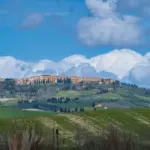 In der Ferne thront die Stadt Pienza auf dem Hügel in der toskanischen Landschaft.