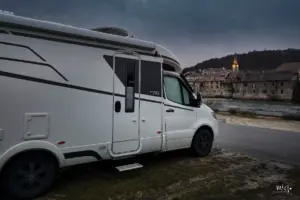 Wohnmobil steht parkiert direkt am Fluss Doubs der viel Wasser führt, im Hintergrund sieht man beim einnachten bereits den erleuchteten Kirchturm.