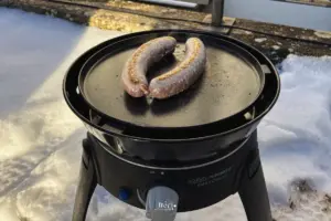 Gasgrill steht im Schnee mit zwei Bratwürsten auf der Grillfläche.