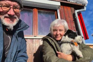 Zwei Menschen und ein Hund geniessen die Wintersonne auf der Terasse vor dem Wohnwagen.