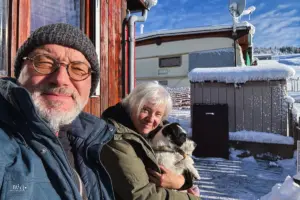 Zwei Menschen und ein Hund geniessen die Wintersonne auf der Terasse vor dem Wohnwagen.