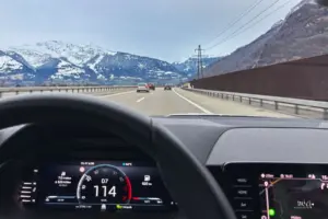 Blick aus dem Cockpit eines fahrenden Autos auf die voraus liegende Strasse und die im Hintergrund ersichtlichen Berge.