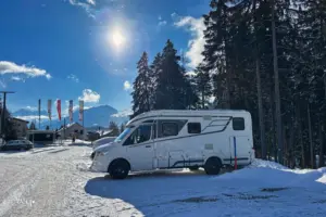 Wohnmobil steht parkiert auf dem verschneiten Parkplatz im Schnee.