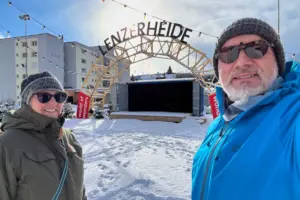 Zwei Menschen stehen vor dem grossen Bogenförmigen Schriftzug Lenzerheide im Schnee.