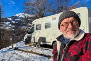 Ein Mann steht vor dem Wohnmobil und macht ein Selfie von sich vor dem Wohnmobil.
