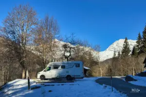 Wohnmobil steht im Schnee auf dem Bergparkplatz dahinter sind die verschneiten Berge zu sehen.