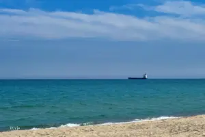 Sicht vom Strand raus aufs weite Meer wo ein grosses Frachtschiff vor Anker liegt.