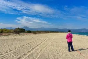 Eine Frau steht alleine am Strand und ihre pinkige Bluse gibt einen leuchtenden Kontrast zum Sand.