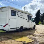 Ein Wohnmobil steht neben der tiefen Schlammpfütze und muss irgendwie um die Pfütze rum wenden.