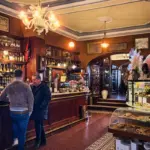 In einer typisch italienischen Bar stehen zwei Männer diskutierend an der Bar und trinken Kaffee.