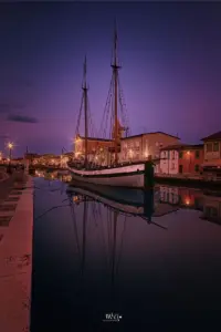 Eines der ausgestellten Schiffe, ein altes Transportschiff, liegt im Wasser mitten in Cesenatico bei schöner Nachtstimmung