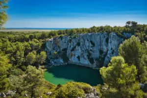 Unterhalb der senkrechten Felswand liegt der Kratersee inmitten des Waldes.