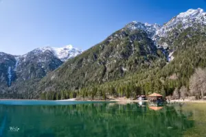 In tiefem grün präsentiert sich der Toblacher See, ein Bergsee in den Dolomiten der eingerahmt wird von den stolzen Bergen die um diese Jahreszeit noch einen weisse Schneekrone tragen.
