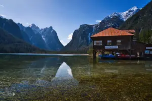 Glatt und ruhig präsentiert sich der Toblacher See, ein Bergsee in den Dolomiten der eingerahmt wird von den stolzen Bergen die um diese Jahreszeit noch einen weisse Schneekrone tragen.