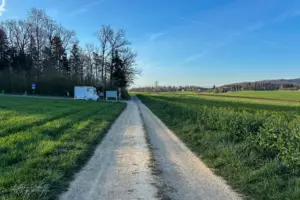 Auf dem kleinen Parkplatz inmitten von Feldern und Wiesen steht ein Wohnmobil parkiert.