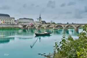 Ein traditionelles Holzboot schwimmt auf der Loire, dahinter ist die Bogenbrücke zu sehen die über die Loire in die Stadt Saumur führt.