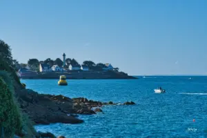 Ein Küstenabschnitt mit einer ins Meer hinausragenden Landzunge die mit Häusern bebaut ist und inmitten der Häuser ragt der Leuchtturm hinaus.