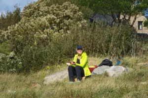 Eine Frau sitzt im grünen auf einem Felsblock und geniesst die Sonne in der Natur.