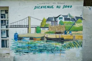 Auf einer Hausfassade ist der kleine Ort Le Bono als Gemälde aufgemalt. Gut zu sehen wie die Stahlseilbrücke die Bucht überspannt.