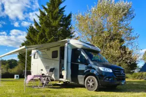 Ein Wohnmobil steht auf der Wiese bei schönstem Herbstwetter und vor dem Wohnmobil sind Tisch und Stühle bereit gestellt um gemütlich draussen an der Sonne zu sitzen.