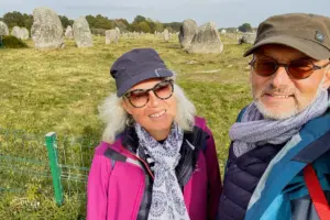 Eine Frau und ein Mann stehen vor einem grossen Feld wo etwa 1100 Steine eine der weltweit grössten Steinreihen bilden.