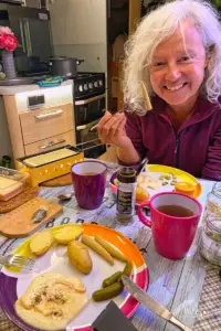 Eine fröhlich lachende Frau sitzt am gedeckten Tisch und freut sich offensichtlich auf ein Raclette.