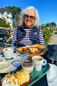 Vor der auf dem Stuhl am Tisch sitzenden Frau steht eine feine Crêpes und Kaffee bereit zum geniessen.