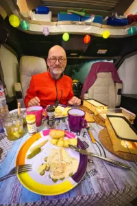 Der Tisch ist gedeckt für ein feines Raclette, auch stimmungsvolles Partylicht ist installiert und der Mann freut sich auf das Raclette.