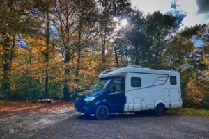 Ein Wohnmobil steht im Herbstwald auf dem Parkplatz.