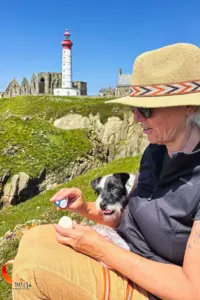 Während die Frau beim Picknick ein Ei mit Salz bestreut, schaut der Hund in der Hoffnung auch etwas abzubekommen erwartungsvoll zu.