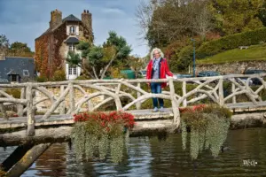 Auf der speziellen Brücke die aussieht als wäre sie aus Holz, ist aber aus kunstvoll geformten Betonästen, steht eine Frau und leuchtet mit ihrem roten Mantel aus der herbstlichen Landschaft.