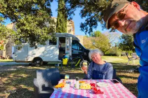 Eine Frau sitzt vor dem Wohnmobil bereit zum anstossen für den Apèro an der Herbstsonne in Südfrankreich.