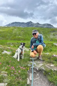 Ein Hund posiert mit seiner Meisterin vor dem Bergpanorama.