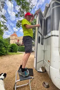 Ein Mann steht auf einem Stuhl und repariert die Türe am Wohnmobil